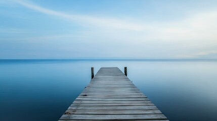 Obraz premium A quiet wooden pier extending out to the horizon, surrounded by the tranquil, still waters of the ocean.