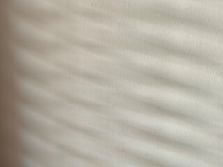 Naklejka premium white fabric texture Light passes through the blinds and hits the cream-white wall, creating patterns and shadows.