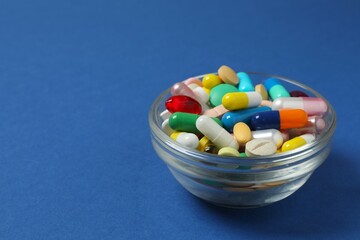 Wooden spoon with pills on blue background, top view