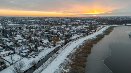 winter landscape. aerial view from drone on snowy city and frozen lake in front of city. beautiful dramatic sunset over water.