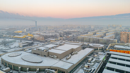 Fototapeta premium winter city landscape from a drone. aerial view of snowy city streets, snowy roofs of buildings on a frosty morning. delicate quiet frosty sunrise over the city.
