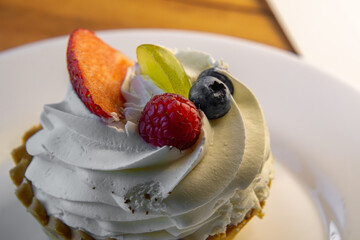 delicious cupcake with fruit and whipped cream on a cake plate. cupcake with strawberries, blueberries, raspberries, grapes. own baking.