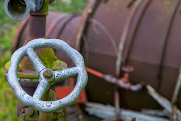 rusty old agricultural machine. rusty steel covered with green moss. metal pipe connections and valves.