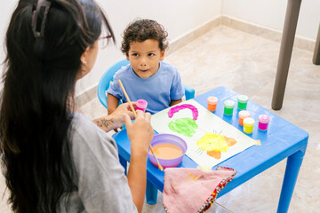 Obraz premium Latin american mom helping son painting at home developing creativity