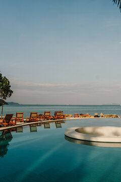 A luxurious infinity pool overlooks the ocean in Koh Lipe, Thailand. Wooden sun loungers line the edge, offering a peaceful and relaxing tropical resort setting with stunning sea views