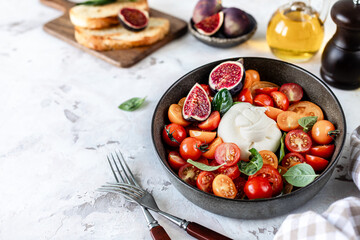 burrata ball with cherry tomatoes, basil leaves, figs and olive oil in a bowl on the table.