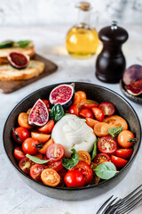 burrata ball with cherry tomatoes, basil leaves, figs and olive oil in a bowl on the table.