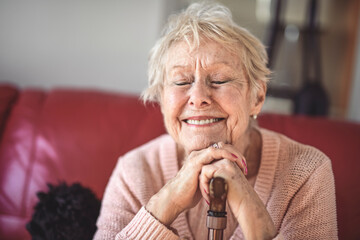 Beautiful senior woman sit on sofa with canes at home