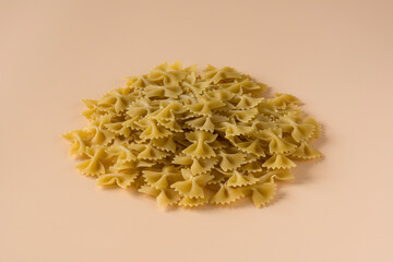 Side view isolated of a raw italian durum wheat farfalle pasta against the orange background .
