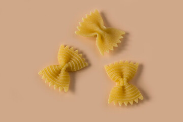 Farfalle, butterfly pasta isolated on light ochre background , top view . Macro shot of three...