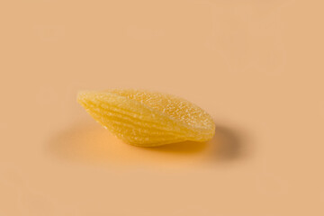 Orecchiette pasta isolated on light ochre background , side view . Macro shot of one isolated raw...