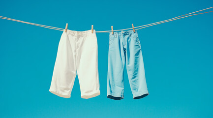 One white pants and one blue trousers hanging on a clothesline, with a bright blue sky background