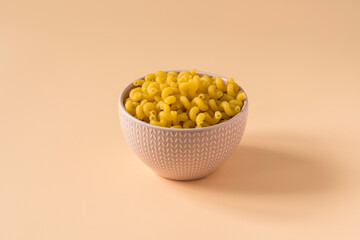 Top view of a porcelain bowl of raw italian durum wheat orecchiette pasta against a light ochre...