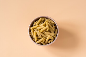 Top view of a bowl of raw italian durum wheat penne lisce pasta against a light ochre background ....