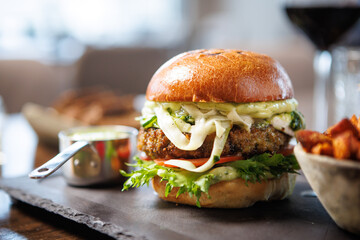 Delicious veggie burger with lettuce, tomato, cheese, and sauce on a toasted bun. Served with a side of sweet potato fries and a small cup of dipping sauce. Perfect for a healthy meal
