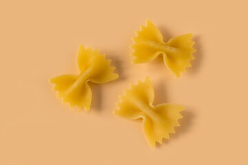 Farfalle, butterfly pasta isolated on light ochre background , top view . Macro shot of three...