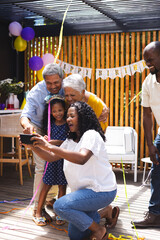 Celebrating birthday in garden, diverse family taking selfie with joyful expressions and decorations