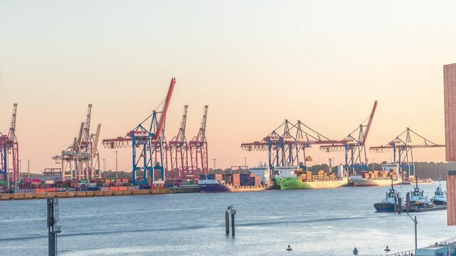 Aerial timelapse of Hamburg cargo port at sunset, showcasing container terminals, cranes and cargo ships on the Elbe River. Boats and vessels pass by, creating a dynamic maritime panorama. Germany