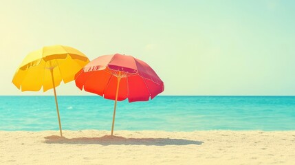 Two colorful umbrellas rest on a sandy beach, overlooking the gentle waves of the ocean under a clear blue sky.