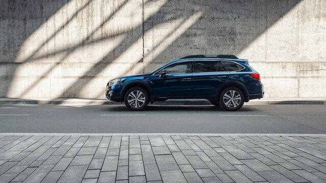 Blue Subaru Outback in front of concrete wall. Side profile view of family wagon crossover on a sunny day, shadows and light beams on grey wall in the back. Kyiv, Ukraine - March 24 2020.