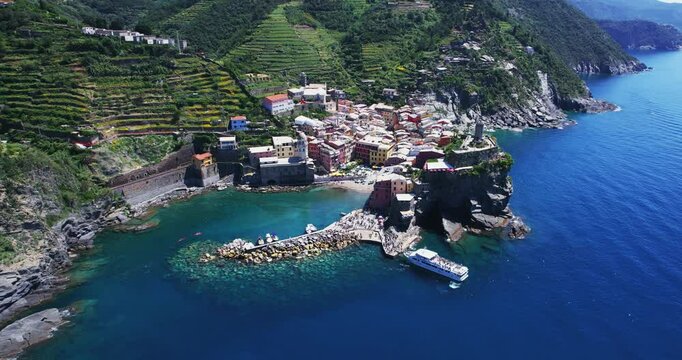 Aerial picturesque view of Vernazza in Cinque Terre, Italy, with anchored tourst boat and colorful houses on rocky cliffs, the iconic Doria Tower