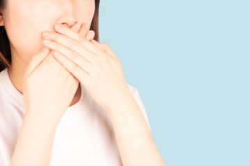 Close up of asian woman covering her mouth with her hands isolated on blue background.