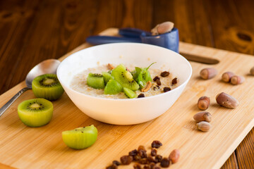 cooked oatmeal with kiwi, honey and nuts in a bowl on a wooden table