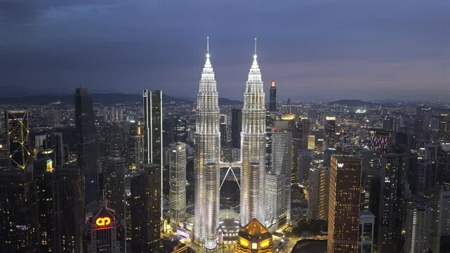 ProRes HDR drone footage of Petronas Towers in downtown Kuala Lumpur, Malaysia as night sets in. Cinematic aerial shot orbiting to the left.