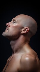 Naklejka premium Bald man looking up, profile view, dark background. Strong, serene expression.