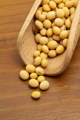 Close em uma concha de madeira com grãos de soja sobre uma mesa de madeira.