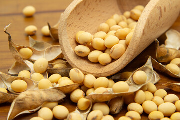 Detalhe de concha de madeira com grãos de soja sobre uma mesa de madeira com vários grãos de soja espalhados.