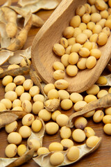 Detalhe de concha de madeira com grãos de soja sobre uma mesa de madeira com vários grãos de soja espalhados.