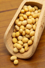 Close em uma concha de madeira com grãos de soja sobre uma mesa de madeira.