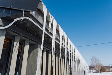 Naklejka premium Icicles are delicately hanging from the side of a building, glistening in the winter light, showcasing the effects of freezing temperatures and the beauty of snow on structures