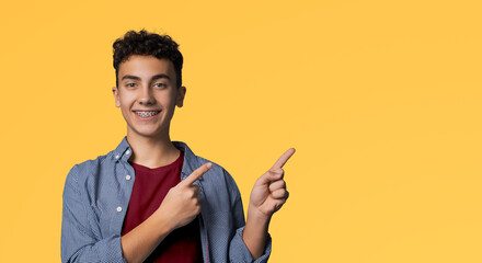 Happy black curly haired man in braces, wear blue shirt, red t-shirt advertise show pointing area...