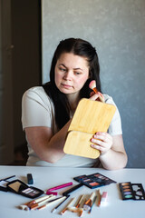 Vertical image of Millennial Caucasian woman doing self make up applying blush on cheeks with make...