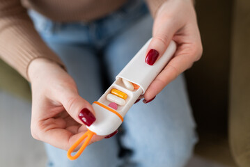 Woman holding a portable pill case with various capsules and tablets. Compact travel medicine...