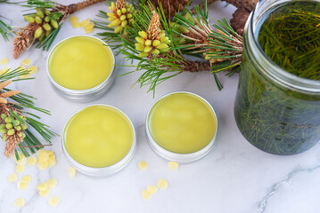 homemade pine needles salve balm in reusable aluminum container  on white marble background.