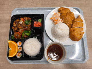 Delicious asian food served on tray with rice, chicken, and sushi rolls bento lunch fast food