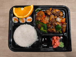 Delicious bento box with teriyaki chicken, rice, sushi and orange slice lunch fast food