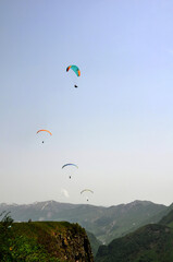 A few bright paragliders soar through the sky above  mountains, embracing the thrill of adventure and freedom