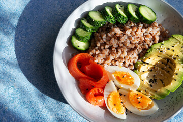 Balanced healthy food on a plate. Buckwheat, boiled egg, cucumber and red fish for breakfast, lunch or dinner.