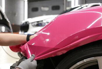 A specialist in wrapping a car with pink-colored vinyl film in the process of work. Car wrapping specialists cover the car with vinyl sheet or film. Car wrapping close-up. Selective focus.