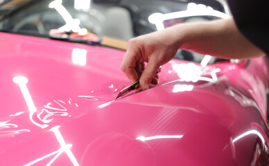A specialist in wrapping a car with pink-colored vinyl film in the process of work. Car wrapping specialists cover the car with vinyl sheet or film. Car wrapping close-up. Selective focus.