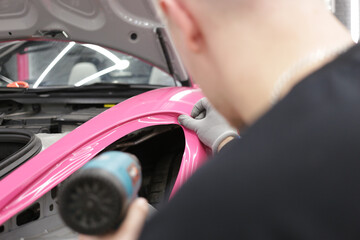 A specialist in wrapping a car with pink-colored vinyl film in the process of work. Car wrapping specialists cover the car with vinyl sheet or film. Car wrapping close-up. Selective focus.