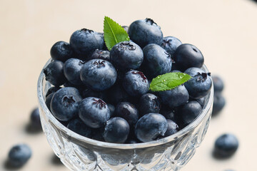Blueberries close-up macro shot served in glass crystal bowl on bright background with water drops.