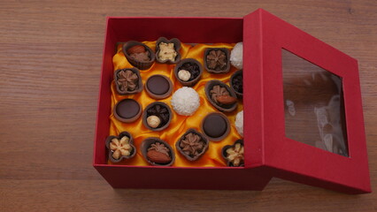 A burgundy box with an open lid full of various chocolates and candies