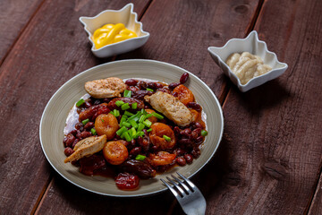 beans stewed with meat and dried fruits and sauce and hummus on a wooden table