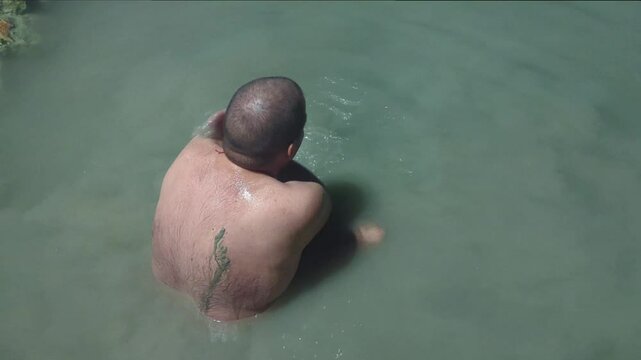 Man in a thermal wild lake applying volcanic healing mud to his body. Rupite, Bulgaria
