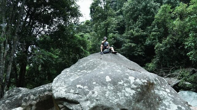 A tourist sits resting on a giant rock in the middle of the jungle